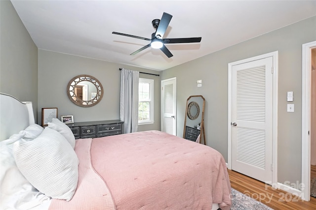 bedroom featuring hardwood / wood-style floors, ceiling fan, and multiple closets