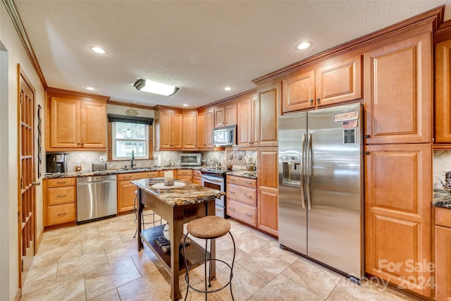 kitchen with appliances with stainless steel finishes, a textured ceiling, light stone countertops, sink, and a center island