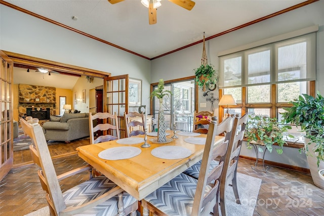 dining space with crown molding, vaulted ceiling, a stone fireplace, and ceiling fan