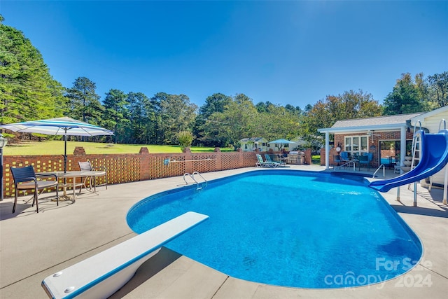 view of swimming pool with a yard, a water slide, a patio area, and a diving board