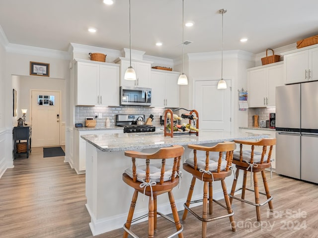 kitchen featuring appliances with stainless steel finishes, decorative light fixtures, a center island with sink, and white cabinets