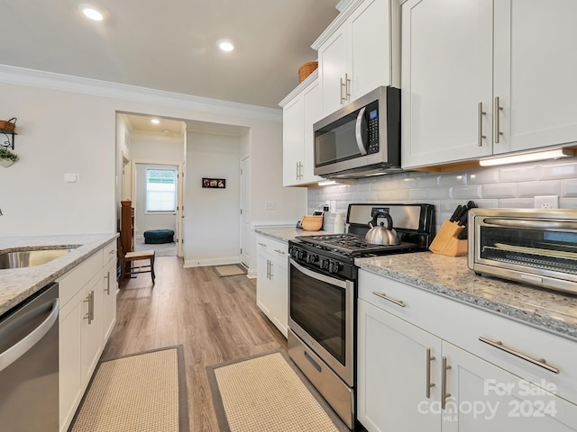 kitchen featuring white cabinets, appliances with stainless steel finishes, light hardwood / wood-style flooring, crown molding, and sink