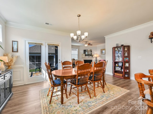 dining space with a wealth of natural light, ornamental molding, wood-type flooring, and ceiling fan with notable chandelier