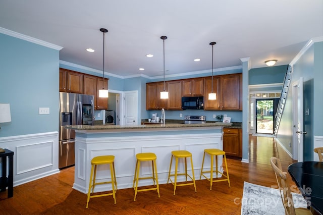 kitchen with a kitchen breakfast bar, ornamental molding, dark stone counters, stainless steel appliances, and a kitchen island with sink