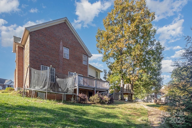 rear view of property featuring a trampoline, a wooden deck, and a lawn