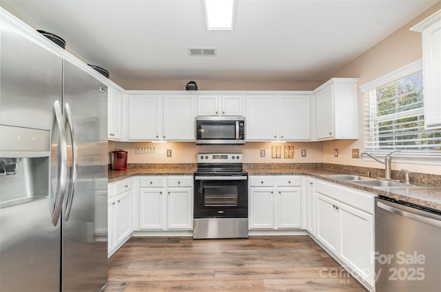 kitchen with sink, light wood-type flooring, white cabinets, and appliances with stainless steel finishes