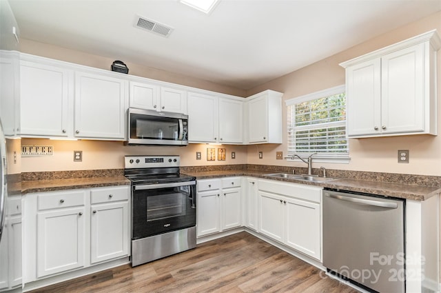 kitchen featuring hardwood / wood-style flooring, white cabinetry, appliances with stainless steel finishes, and sink