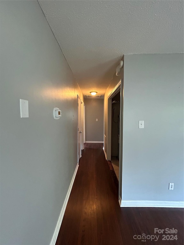 hall with a textured ceiling and dark wood-type flooring