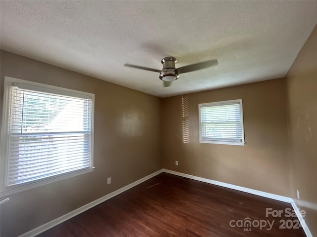 spare room with a textured ceiling, ceiling fan, dark wood-type flooring, and a wealth of natural light