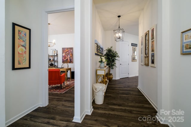 hallway with vaulted ceiling, dark hardwood / wood-style floors, and an inviting chandelier