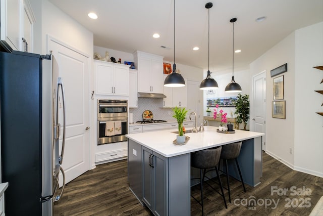 kitchen with appliances with stainless steel finishes, decorative light fixtures, white cabinetry, tasteful backsplash, and a center island with sink