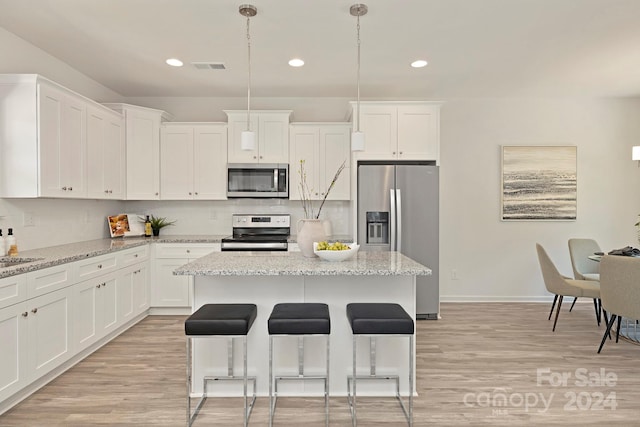 kitchen featuring white cabinets, light stone countertops, stainless steel appliances, and pendant lighting