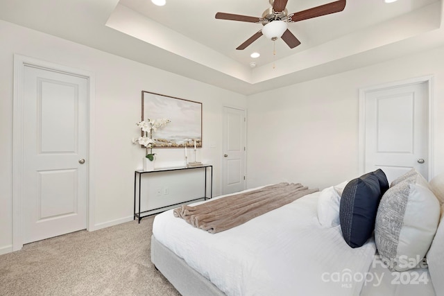 bedroom featuring ceiling fan, a raised ceiling, and light colored carpet