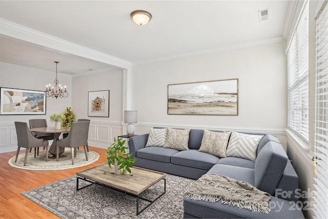 living room featuring wood-type flooring, crown molding, and a notable chandelier