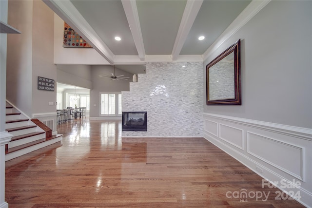 unfurnished living room featuring beamed ceiling, wood-type flooring, crown molding, a fireplace, and ceiling fan