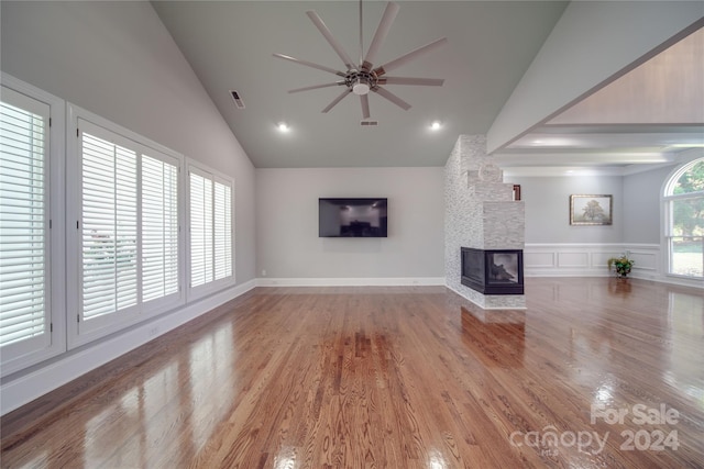 unfurnished living room with ceiling fan, lofted ceiling, a multi sided fireplace, and hardwood / wood-style floors