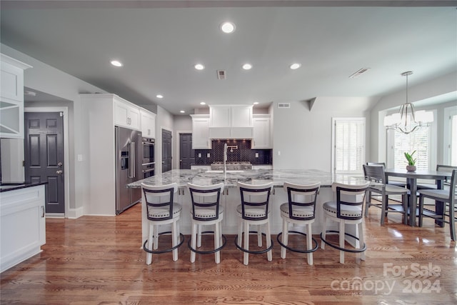 kitchen featuring white cabinets, tasteful backsplash, an inviting chandelier, a kitchen island with sink, and dark wood-type flooring