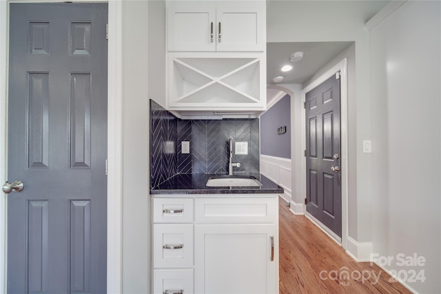 kitchen featuring backsplash, dark stone counters, sink, light wood-type flooring, and white cabinetry