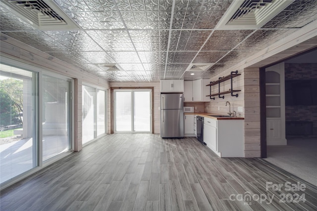 kitchen featuring stainless steel fridge, white cabinetry, wood walls, light hardwood / wood-style floors, and sink