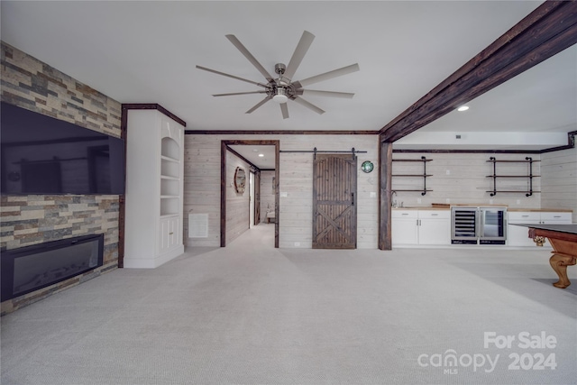 unfurnished living room with light colored carpet, beam ceiling, wood walls, and a barn door