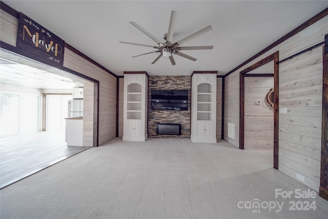 unfurnished living room with ornamental molding, wooden walls, light colored carpet, and ceiling fan