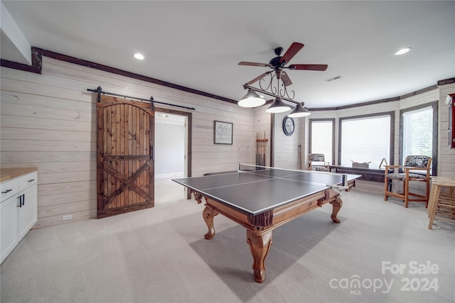 game room with ceiling fan, a barn door, light carpet, and wood walls