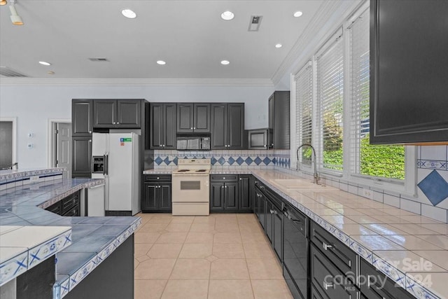 kitchen featuring white appliances, sink, ornamental molding, tile counters, and decorative backsplash