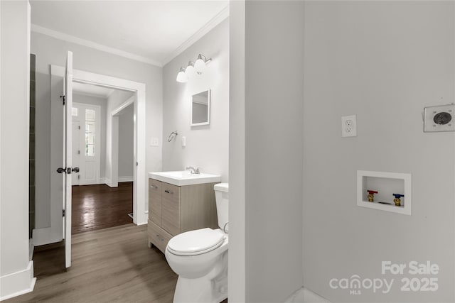 half bathroom with toilet, wood finished floors, vanity, baseboards, and ornamental molding