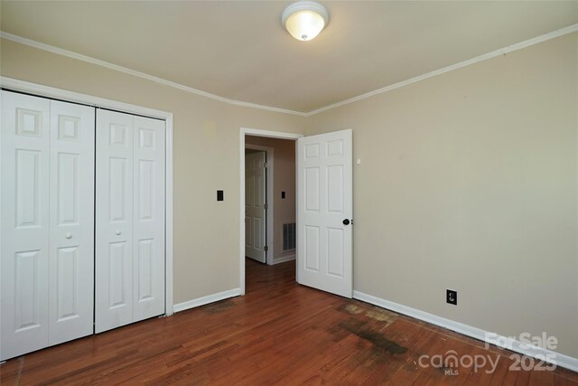 unfurnished bedroom with baseboards, wood finished floors, ornamental molding, and a closet