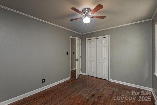 unfurnished bedroom featuring baseboards, dark wood-style floors, a closet, ornamental molding, and ceiling fan