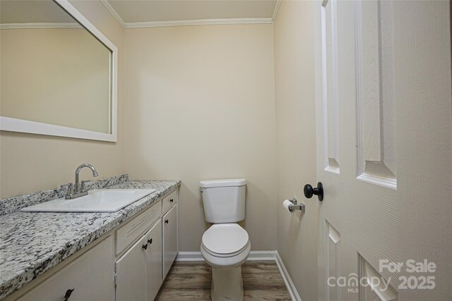 bathroom with wood finished floors, toilet, vanity, ornamental molding, and baseboards