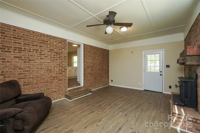 living room featuring wood finished floors, ceiling fan, a fireplace, brick wall, and baseboards