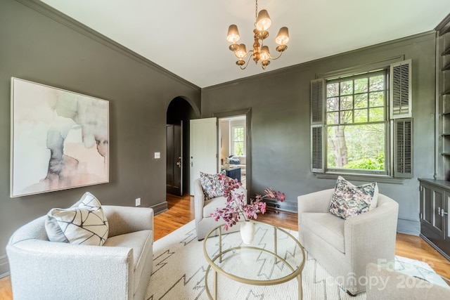 living room featuring light wood-type flooring, ornamental molding, arched walkways, and a chandelier