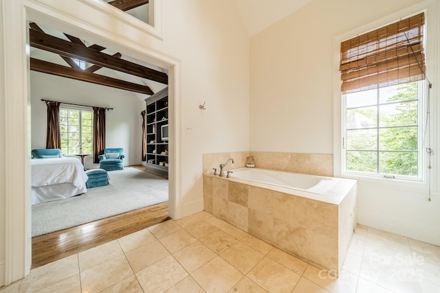 ensuite bathroom featuring a wealth of natural light, beam ceiling, tile patterned flooring, and a garden tub