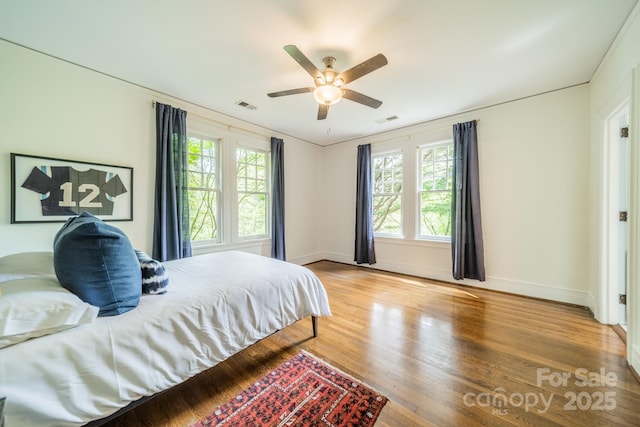bedroom featuring visible vents, ceiling fan, baseboards, and wood finished floors