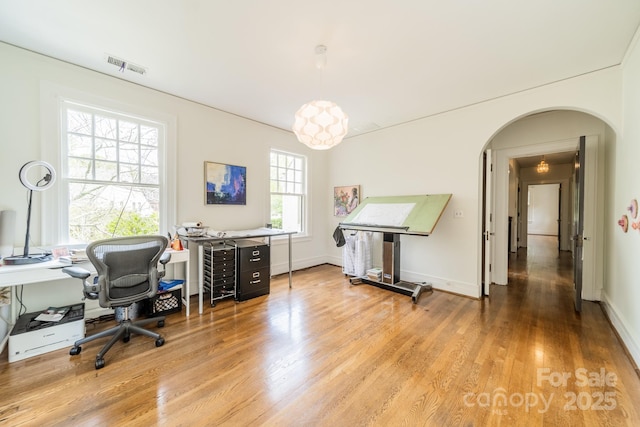 office area featuring light wood finished floors, baseboards, visible vents, and arched walkways