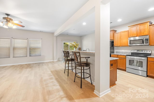 kitchen featuring ceiling fan, stainless steel appliances, a kitchen breakfast bar, light stone counters, and light hardwood / wood-style floors