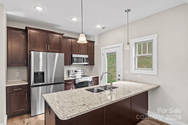 kitchen featuring light stone counters, stainless steel appliances, hanging light fixtures, sink, and kitchen peninsula