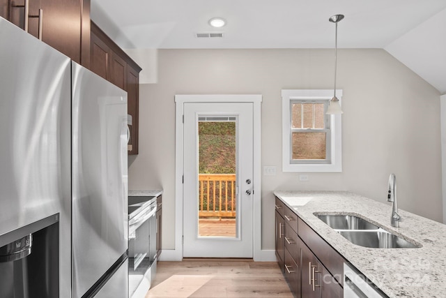 kitchen with sink, light stone counters, appliances with stainless steel finishes, decorative light fixtures, and light hardwood / wood-style flooring