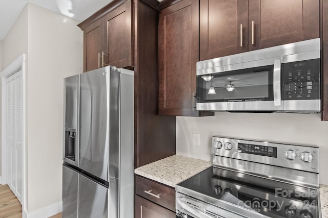 kitchen with light stone counters, dark brown cabinets, light wood-type flooring, and appliances with stainless steel finishes