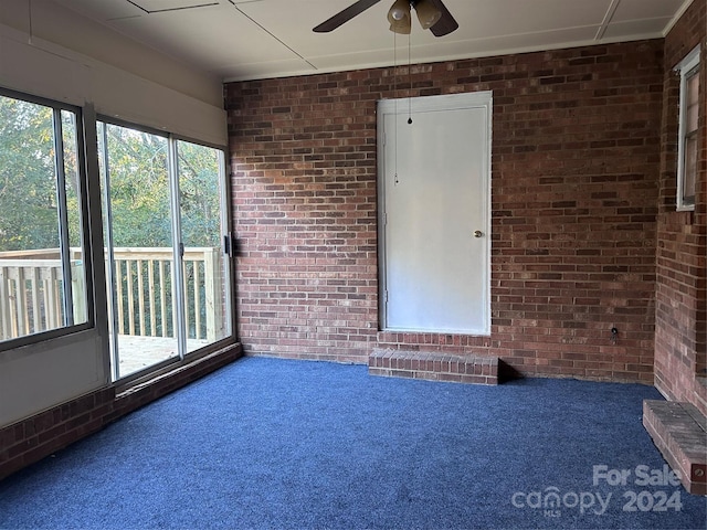 unfurnished room featuring ceiling fan, brick wall, and carpet flooring