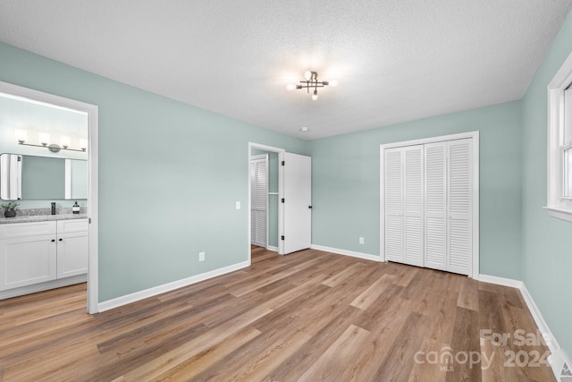 unfurnished bedroom featuring a closet, a textured ceiling, connected bathroom, and light wood-type flooring