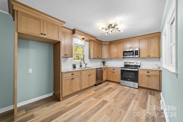 kitchen with backsplash, sink, light wood-type flooring, a chandelier, and appliances with stainless steel finishes