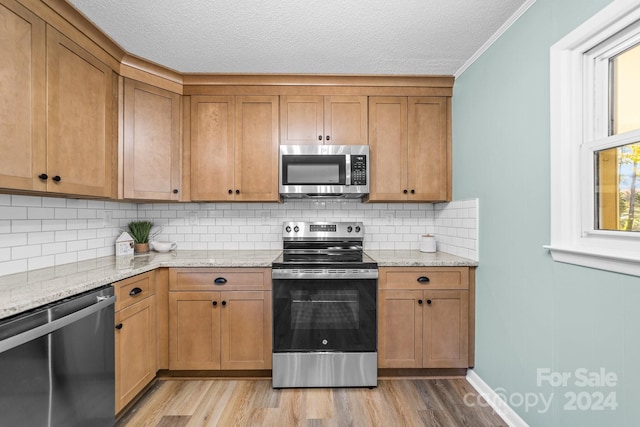 kitchen featuring crown molding, appliances with stainless steel finishes, light hardwood / wood-style flooring, and light stone counters