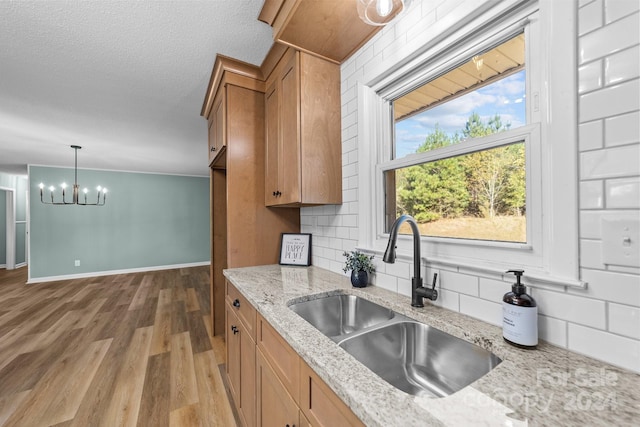 kitchen with light hardwood / wood-style flooring, hanging light fixtures, sink, light stone counters, and tasteful backsplash