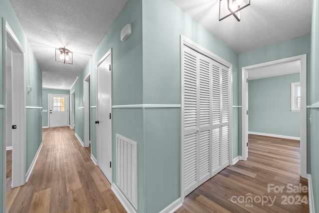 hall with a textured ceiling and light wood-type flooring