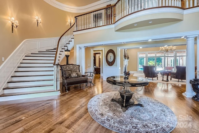 foyer with hardwood / wood-style flooring, decorative columns, a high ceiling, crown molding, and a notable chandelier