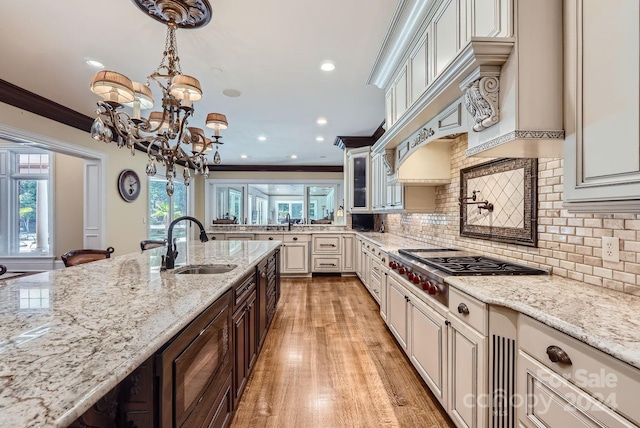 kitchen featuring hanging light fixtures, light stone counters, ornamental molding, light hardwood / wood-style floors, and sink