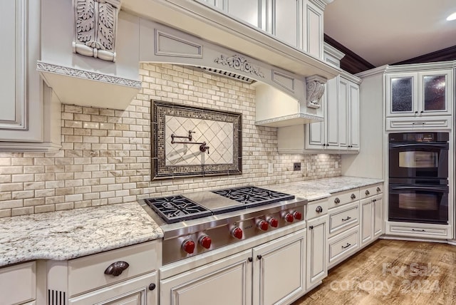 kitchen with backsplash, stainless steel gas stovetop, light stone counters, light hardwood / wood-style flooring, and black double oven