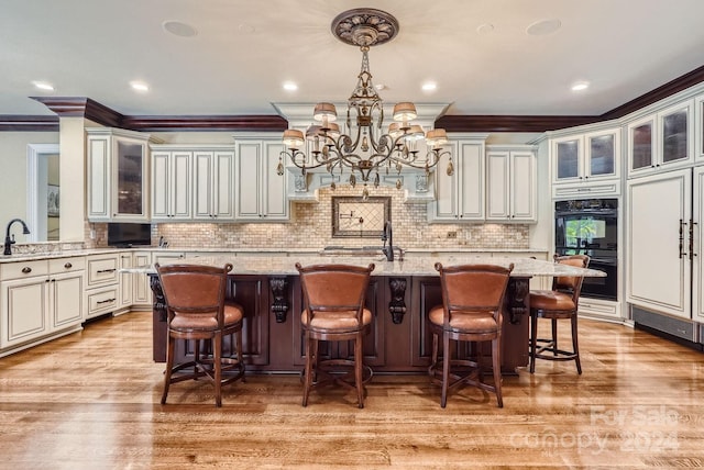 kitchen with light hardwood / wood-style flooring, ornamental molding, light stone countertops, and a center island with sink